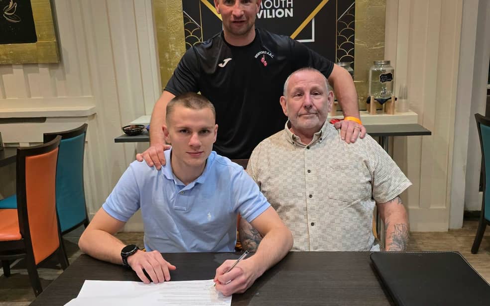 Neo signing his professional contract with coach and manager at a table