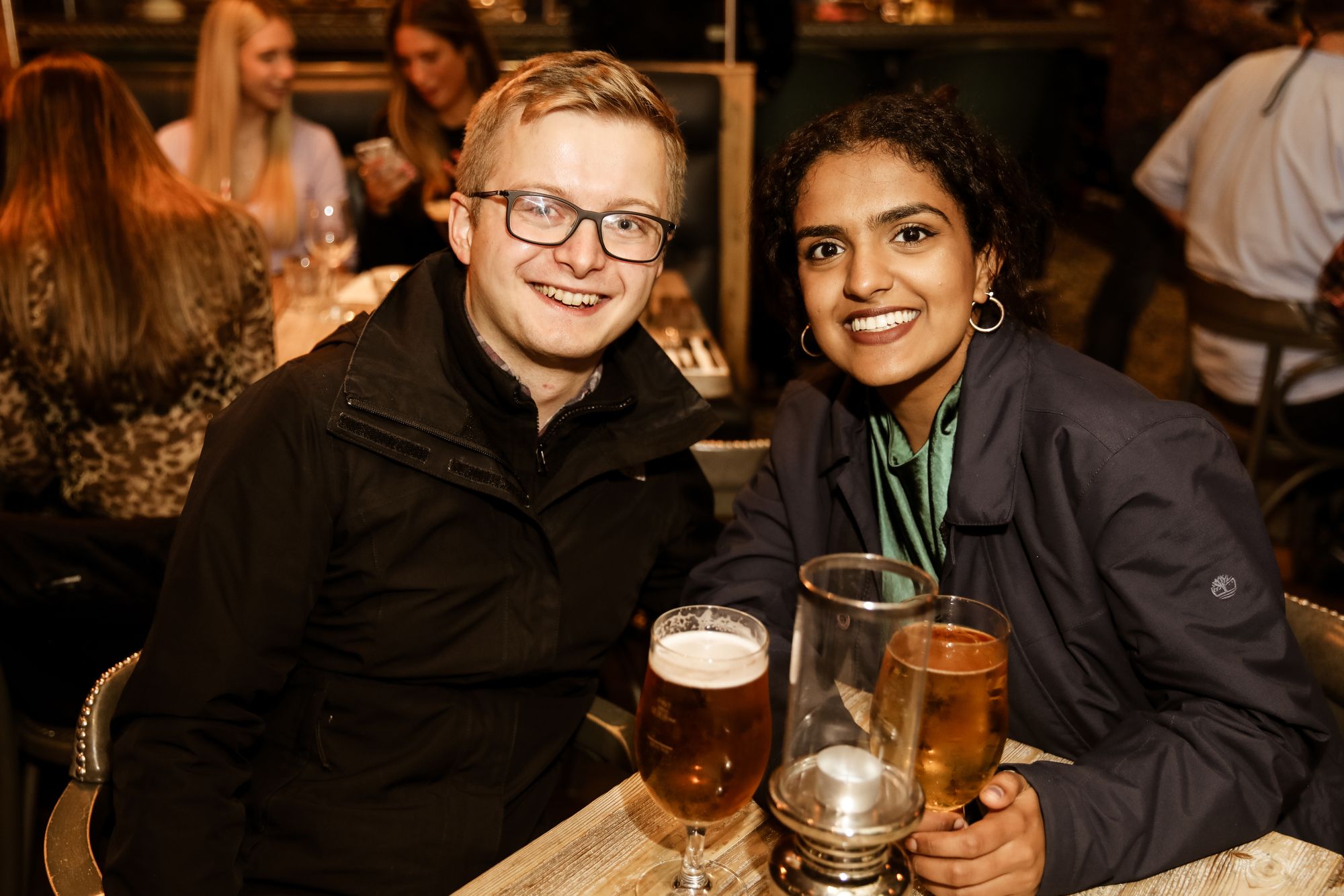 Man and woman with their drinks, sat at table and smiling for photo