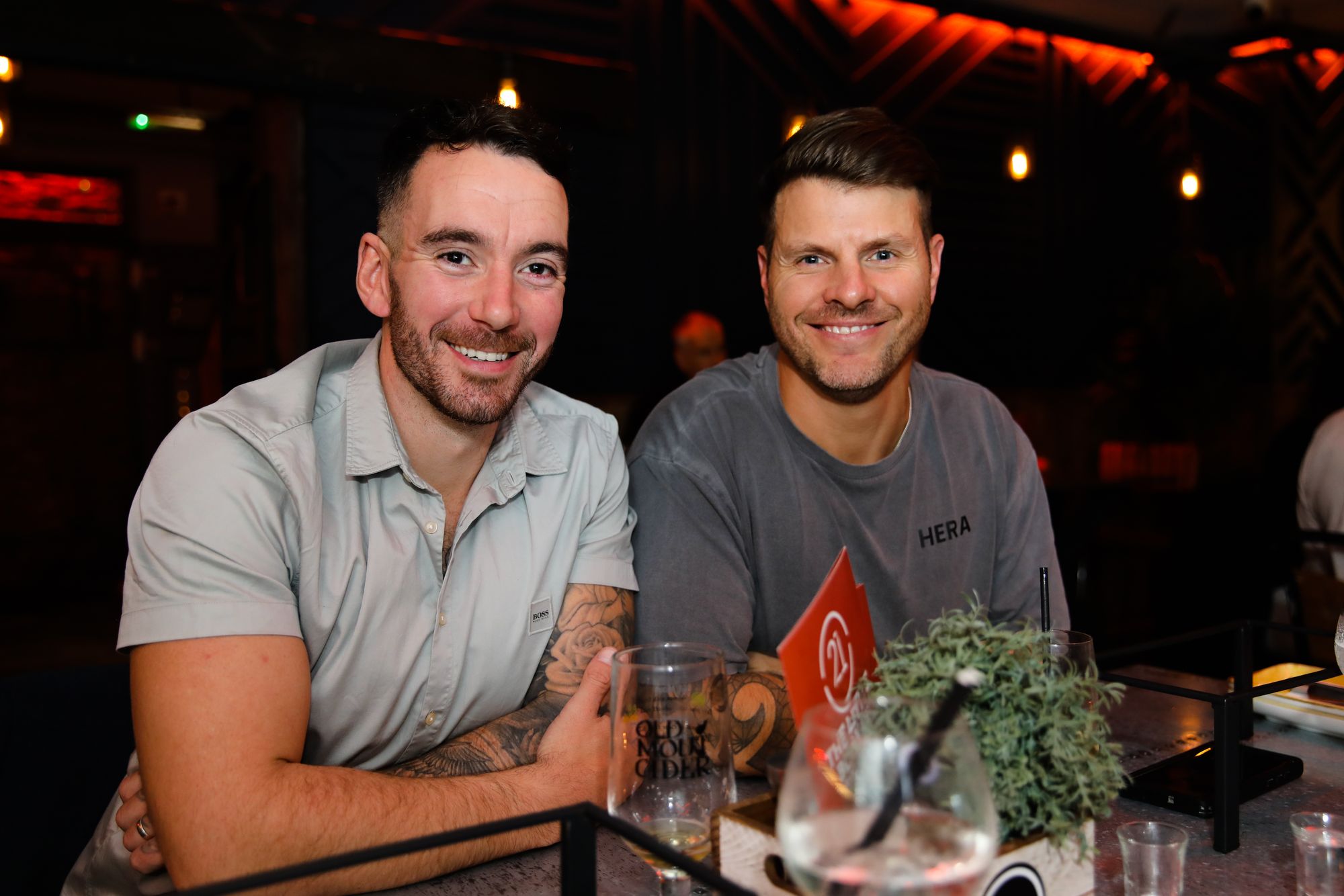 Two bearded young men sat at the bar and smiling at the camera