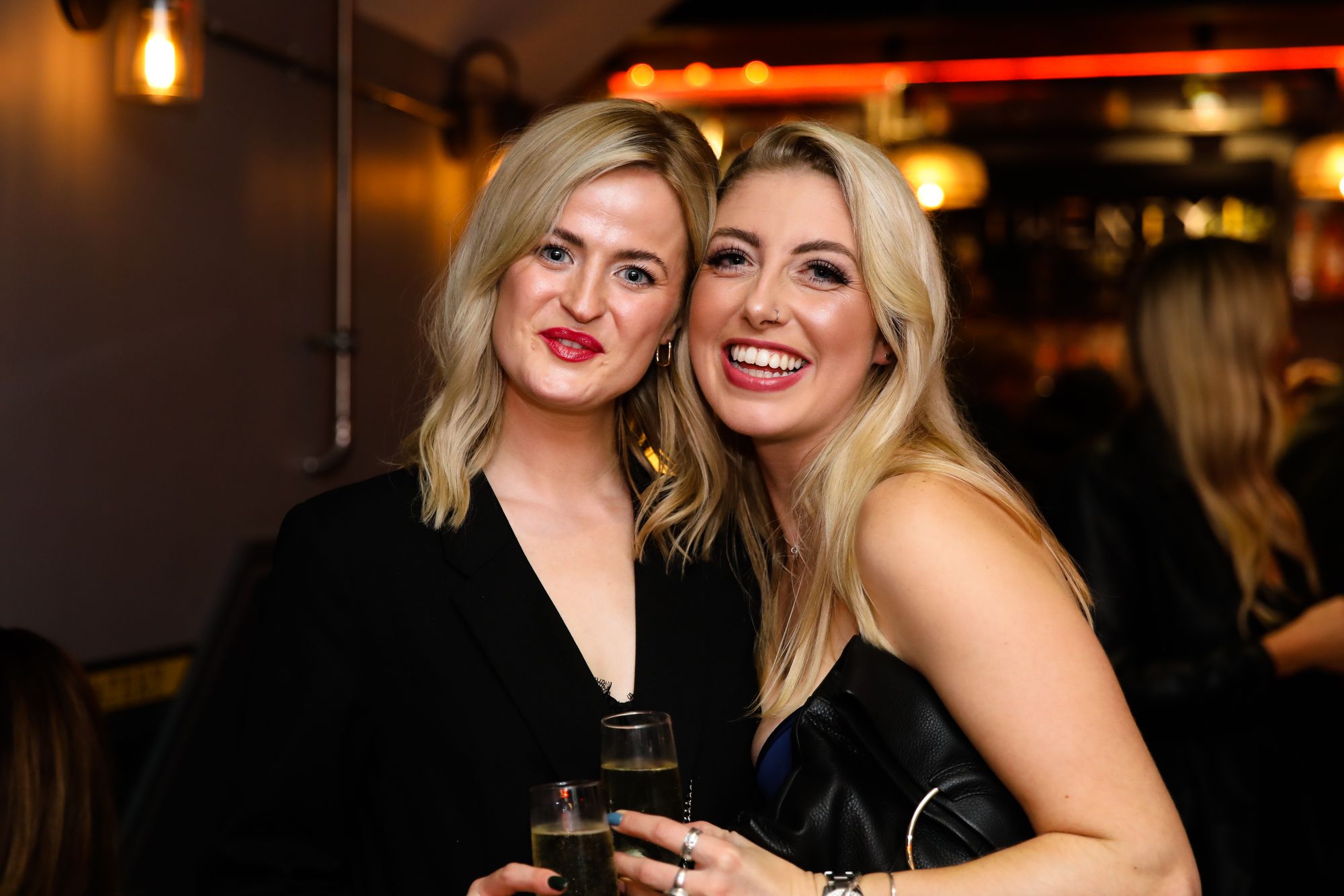 Two blonde women wearing black tops, both smiling at the camera