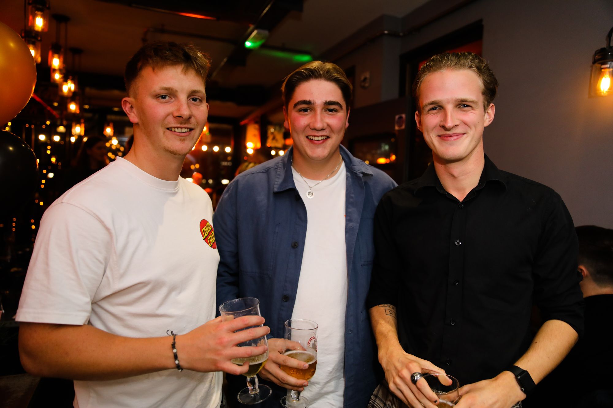 Three young men in T-shirts and holding beers smiling at the camera